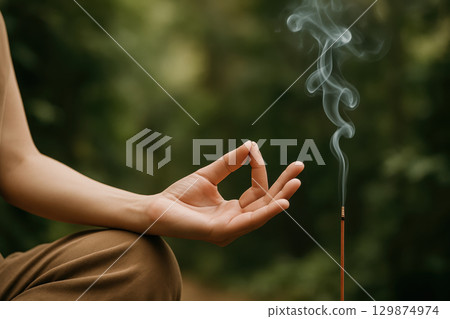 Peaceful hand in mudra gesture with incense stick smoke curling in natural green background creating calm and serene atmosphere for meditation and relaxation practice Peaceful hand in mudra gesture with incense stick smoke curling in natural green background creating calm and serene atmosphere for meditation and relaxation practice 129874974
