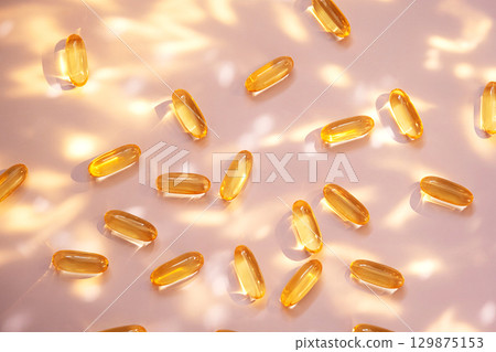 Yellow fish oil capsules on light pink background with sun glare and shadows. Yellow fish oil capsules on light pink background with sun glare and shadows. 129875153