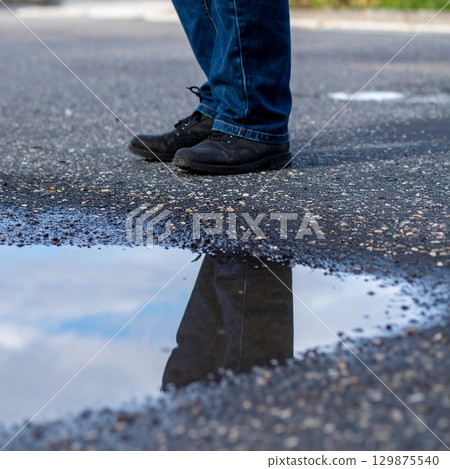 Feet in shoes standing close to a puddle with reflections 129875540