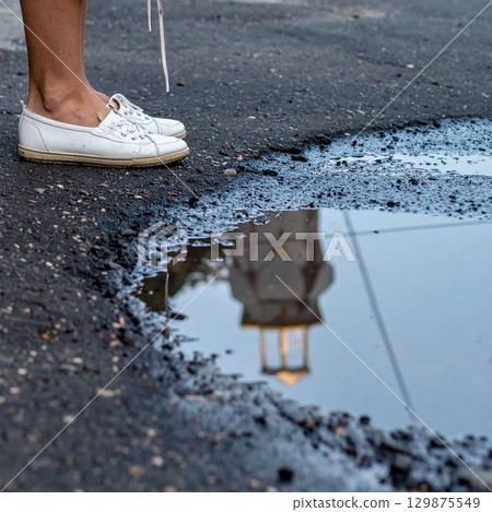 Feet in shoes standing close to a puddle with reflections 129875549