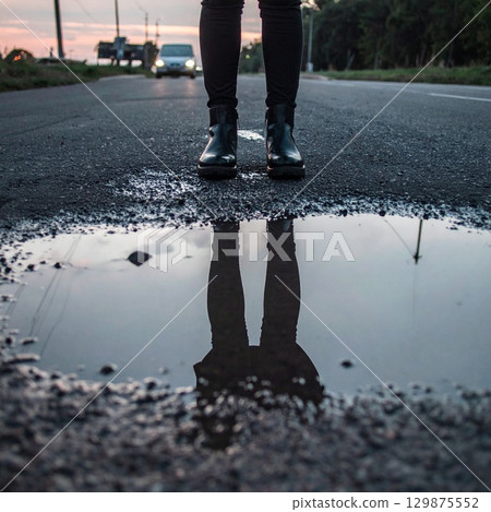 Feet in shoes standing close to a puddle with reflections 129875552
