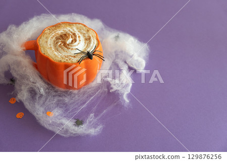 Halloween themed flat lay with a pumpkin latte and spiderwebs on a purple background. Halloween themed flat lay with a pumpkin latte and spiderwebs on a purple background. 129876256
