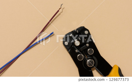 Wire stripper lies next to two cut electrical wires red and blue on beige background. Wire stripper lies next to two cut electrical wires red and blue on beige background. 129877373