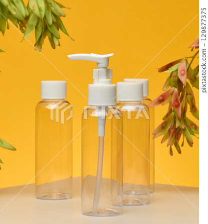 Transparent cosmetic bottles with white caps pump, flip-top. Yellow background Transparent cosmetic bottles with white caps pump, flip-top. Yellow background 129877375