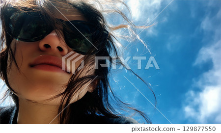 藍天下戴著太陽眼鏡的女人的肖像 129877550