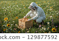 Beekeeper in a white suit working with a beehive in a field, surrounded by flowers and bees 129877592