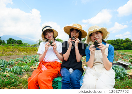 Japanese girls wearing straw hats sit holding white rice balls on a summer plateau 129877702