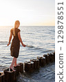 Cute adorable blond teenager happy kid girl walking by wooden breakwater posts at Baltic sea scenic warm summer sunset light. Balancing reflects challenges, choices and uncertainties of growing up 129878551