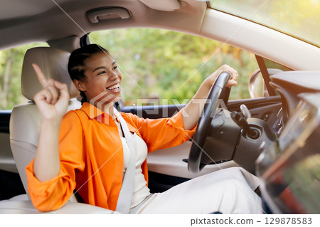 Joyful black woman dancing in the car, pointing up with enthusiasm Joyful black woman dancing in the car, pointing up with enthusiasm 129878583