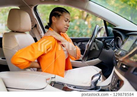 Black woman suffering pain, touching back and shoulder while sitting in car 129878584