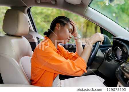 Tired black woman sitting in car, head resting on hand, eyes closed Tired black woman sitting in car, head resting on hand, eyes closed 129878595