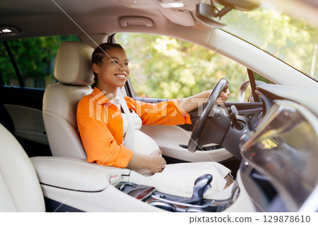 Young African American pregnant woman joyfully driving car, hand on belly Young African American pregnant woman joyfully driving car, hand on belly 129878610