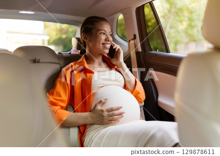 Pregnant black woman in backseat talking on phone while touching belly 129878611