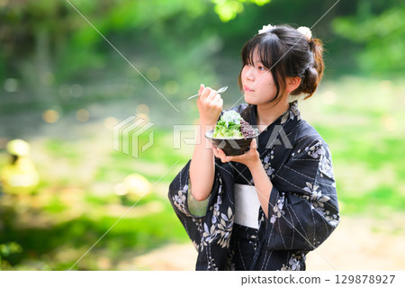 A scene of a Japanese elementary school girl wearing a yukata eating shaved ice at a lake in the highlands in summer 129878927