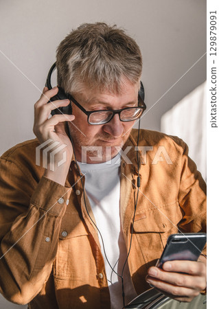 middle-aged man listening to music on headphones while using smartphone indoors. closeup. 129879091