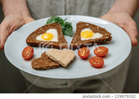 heart-shaped fried eggs served on bread fresh tomatoes for festive breakfast experience. closeup. 129879102