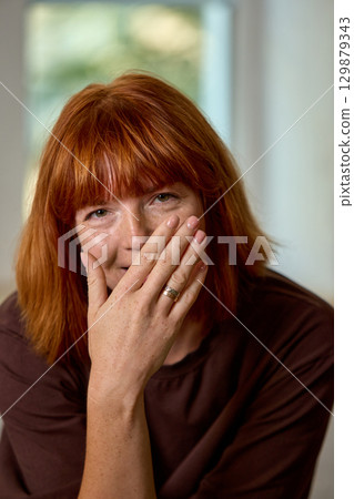 Red haired woman covering smile with hand showing ring indoors Red haired woman covering smile with hand showing ring indoors 129879343
