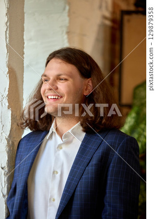 Young man in suit standing near window with joyful smile Young man in suit standing near window with joyful smile 129879358