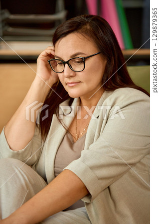 Woman in glasses sitting with thoughtful expression 129879365