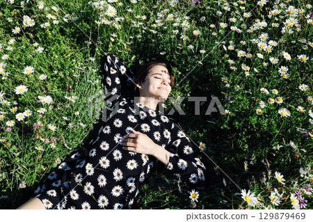 Beautiful woman in summer dress lying on a field of daisy flowers 129879469
