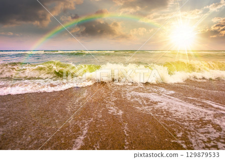 sea tide before storm at sunset. wave splash with foam on wet sandy beach in evening light. windy weather on velvet season. dramatic seascape background 129879533