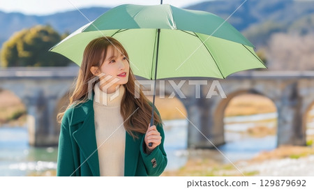 A beautiful woman holding an umbrella and gazing into the distance at a tourist spot 129879692