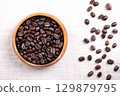 Roasted  Arabica coffee beans, in a wooden bowl, on linen. Dark brown roasted seeds of berries from Coffea arabica, also known as Arabian, mountain or Arabica coffee. Close-up, from above. Food photo. 129879795