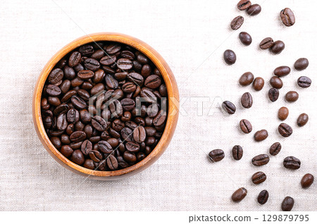 Roasted Arabica coffee beans, in a wooden bowl, on linen. Dark brown roasted seeds of berries from Coffea arabica, also known as Arabian, mountain or Arabica coffee. Close-up, from above. Food photo. Roasted Arabica coffee beans, in a wooden bowl, on linen. Dark brown roasted seeds of berries from Coffea arabica, also known as Arabian, mountain or Arabica coffee. Close-up, from above. Food photo. 129879795