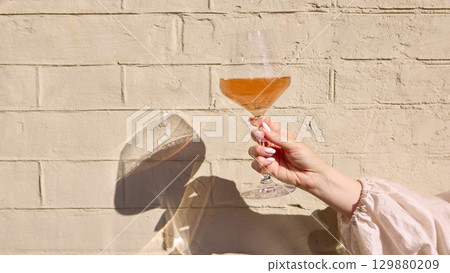 Rose wine glass in hand with sunlight and soft shadow on wall 129880209