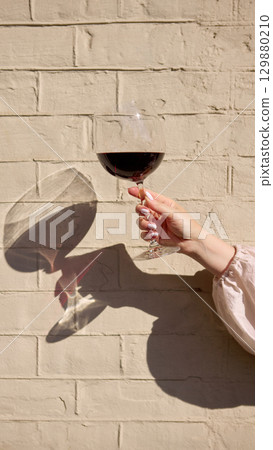 Red wine glass in hand with sunlight and shadow on wall Red wine glass in hand with sunlight and shadow on wall 129880210