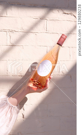 Rose wine bottle with blank round label in hand against brick wall, mockup for ad, text 129880238