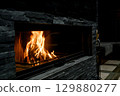 Cozy living room with a modern stone fireplace, warm flames flickering inside, creating an inviting and tranquil atmosphere. 129880277