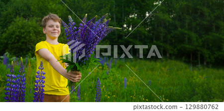 In a vibrant meadow of purple lupines, a happy boy wearing yellow enjoys the sunshine, his smile reflecting pure joy and carefree spirit. In a vibrant meadow of purple lupines, a happy boy wearing yellow enjoys the sunshine, his smile reflecting pure joy and carefree spirit. 129880762