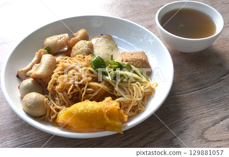 dry yellow egg noodles dory fish and fishball with bean sprout topping crispy dumpling on plate with soup dry yellow egg noodles dory fish and fishball with bean sprout topping crispy dumpling on plate with soup 129881057
