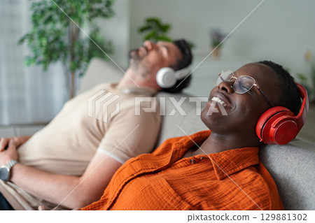 Couple relaxing on sofa listening to music with headphones Couple relaxing on sofa listening to music with headphones 129881302