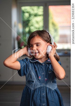 Young girl listening to music with headphones at home Young girl listening to music with headphones at home 129881364