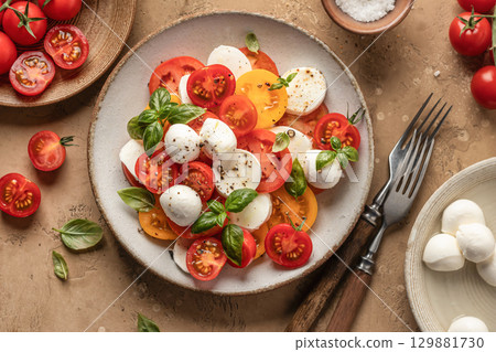 Caprese salad with sliced tomatoes, mozzarella, basil, olive oil close up on brown textured background. Top view Caprese salad with sliced tomatoes, mozzarella, basil, olive oil close up on brown textured background. Top view 129881730