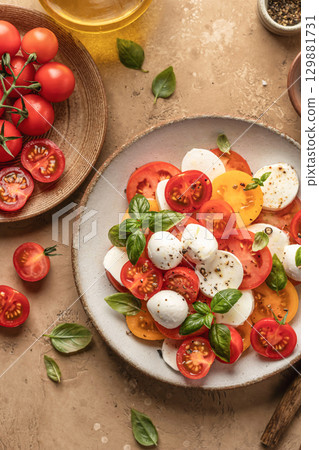 Caprese salad with sliced tomatoes, mozzarella, basil, olive oil close up on brown textured background. Top view Caprese salad with sliced tomatoes, mozzarella, basil, olive oil close up on brown textured background. Top view 129881731