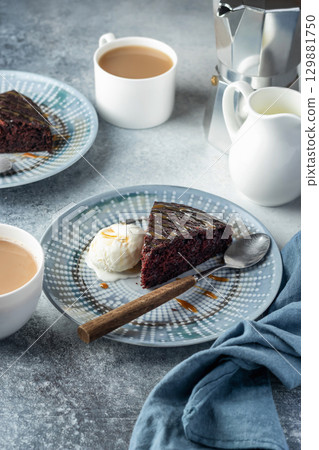 A piece of chocolate brownie cake on blue plate served with a scoop of ice cream and caramel topping with coffee A piece of chocolate brownie cake on blue plate served with a scoop of ice cream and caramel topping with coffee 129881750