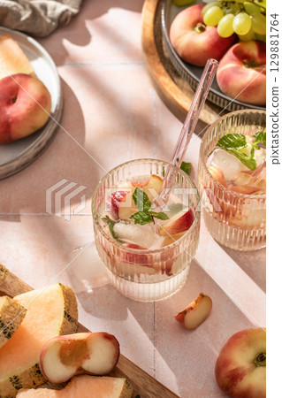 Summer cold drinks: homemade iced peach lemonade with mint in glass on pink tile background in bright morning light Summer cold drinks: homemade iced peach lemonade with mint in glass on pink tile background in bright morning light 129881764