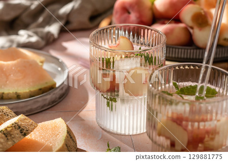 Summer cold drinks: homemade iced peach lemonade with mint in glass on pink tile background in bright morning light Summer cold drinks: homemade iced peach lemonade with mint in glass on pink tile background in bright morning light 129881775