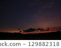Late twilight view of a flooded rice field under a darkening sky. Clouds drift across deep purple and orange hues, with silhouettes of hills and trees adding a calm, moody atmosphere. 129882318
