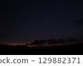 A quiet rural scene at nightfall with deep shadows over a rice field. The last light of sunset casts a subtle orange and purple hue behind dark clouds and silhouetted hills. 129882371