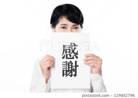 A shy senior woman holding a piece of paper with the word "thank you" written on it 129882796