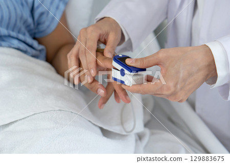 A healthcare professional is using a fingertip pulse oximeter on a patient's finger in a hospital room. This procedure is crucial for assessing respiratory health and blood oxygen level. Close up 129883675