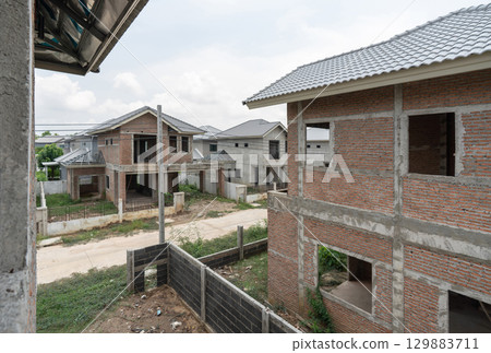 Newly built house line a quiet road in a developing suburban neighborhood. Construction is ongoing, with clear skies overhead and greenery surrounding the area, reflecting a growing community. 129883711