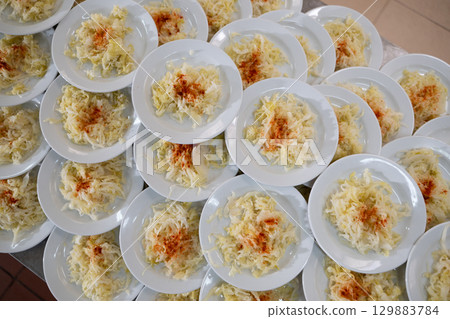 Overhead view of many plates filled with cabbage salad garnished with paprika, catering and food service concept 129883784