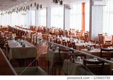 Empty restaurant dining hall with arranged tables and chairs 129883795