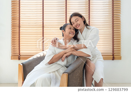 In a cozy spa, a mother and daughter share joyful moment wrapped in soft robe, surrounded by natural light and wooden texture. In a cozy spa, a mother and daughter share joyful moment wrapped in soft robe, surrounded by natural light and wooden texture. 129883799