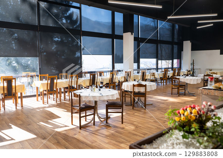Restaurant interior with large sunlit windows and wooden chairs Restaurant interior with large sunlit windows and wooden chairs 129883808